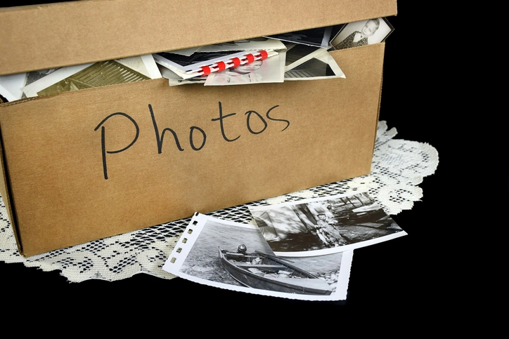Cardboard box labeled photos with black-and-white printed photographs nearby.